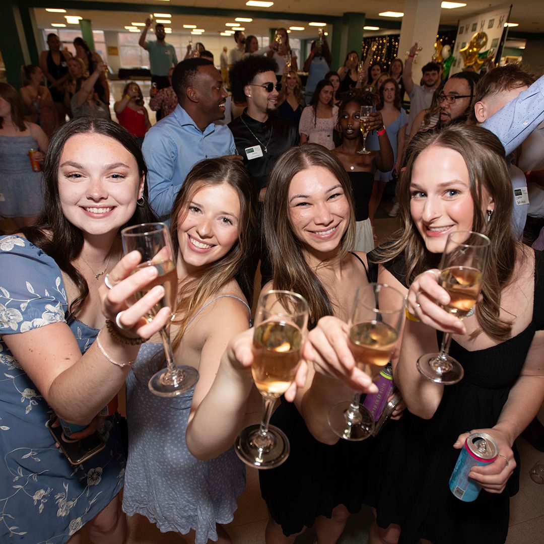 Smiling people holding champagne glasses look at the camera.