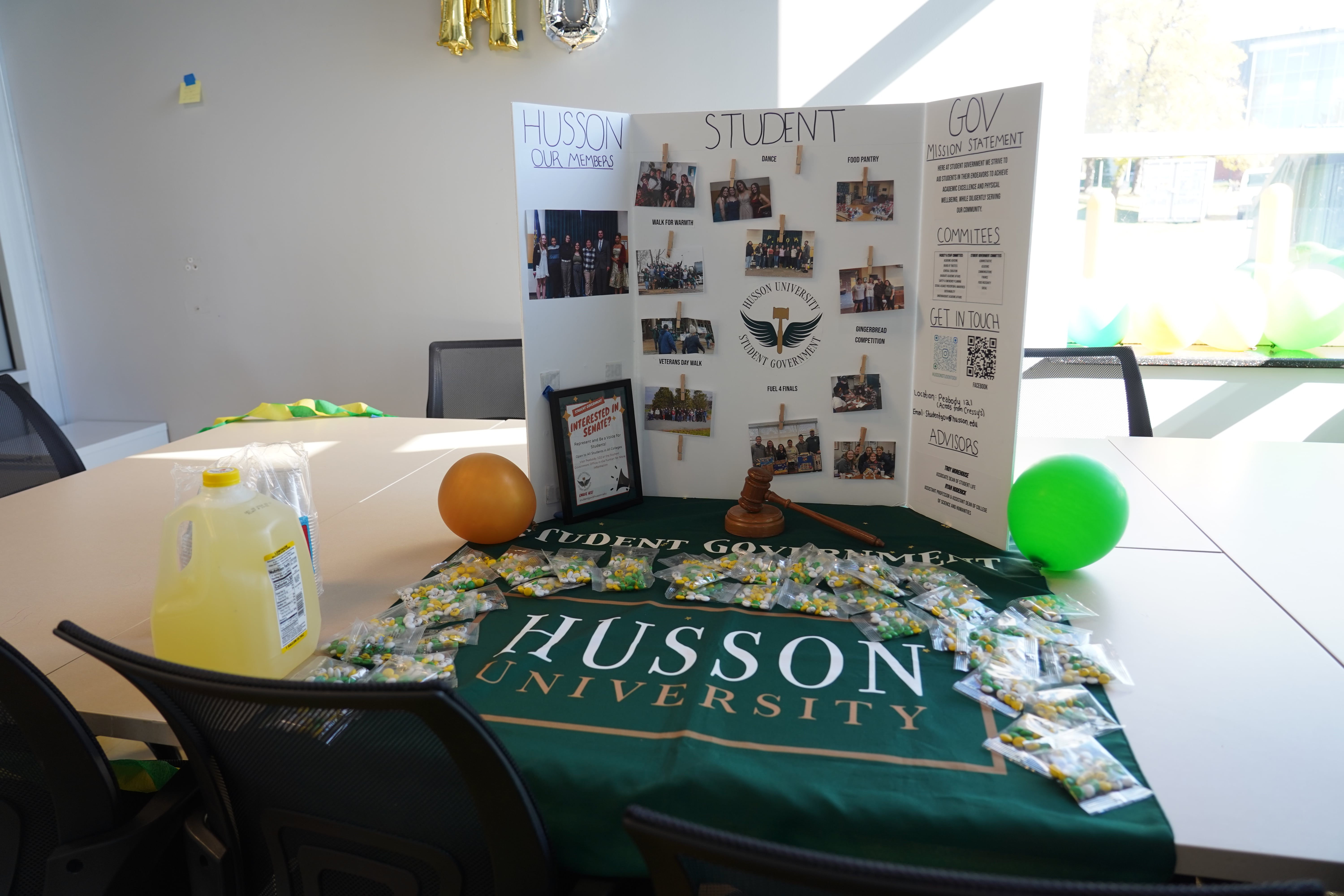  A poster board display with pictures and sentences describing Student Government sits on a long table in Husson University Student Government's new office.