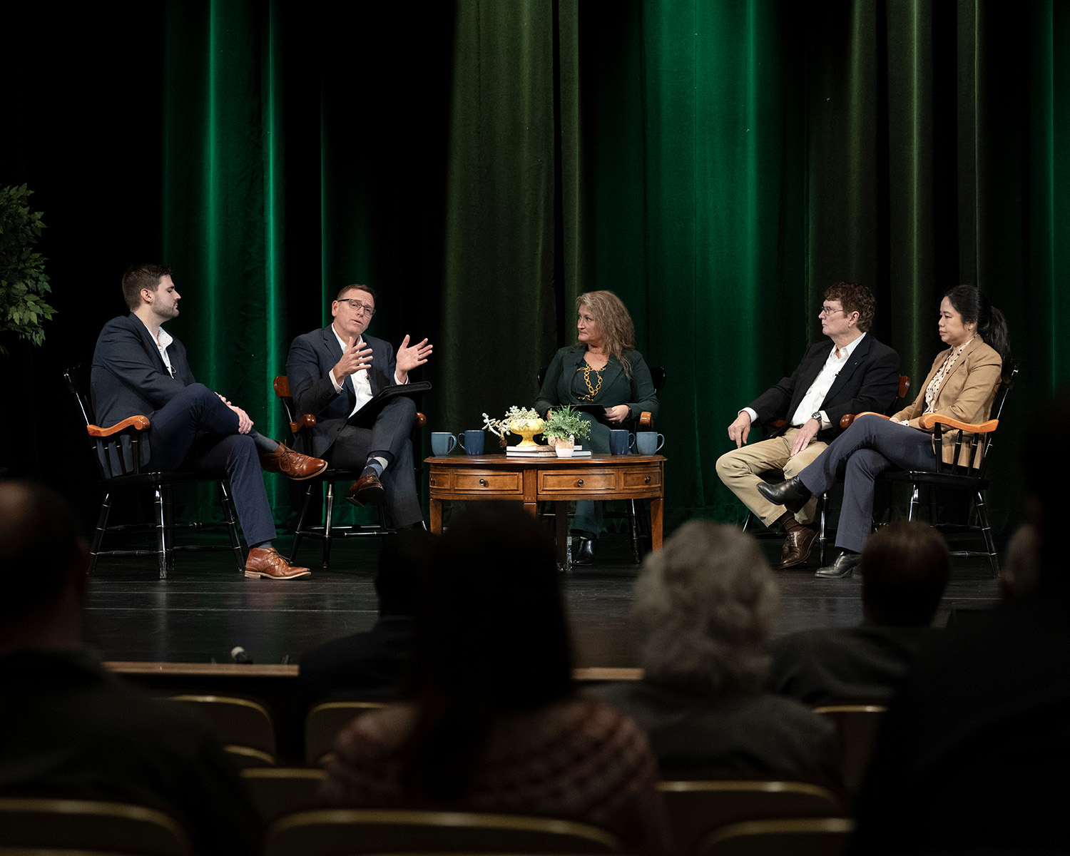 Five people sit in captain's chairs on the stage of a theatre.