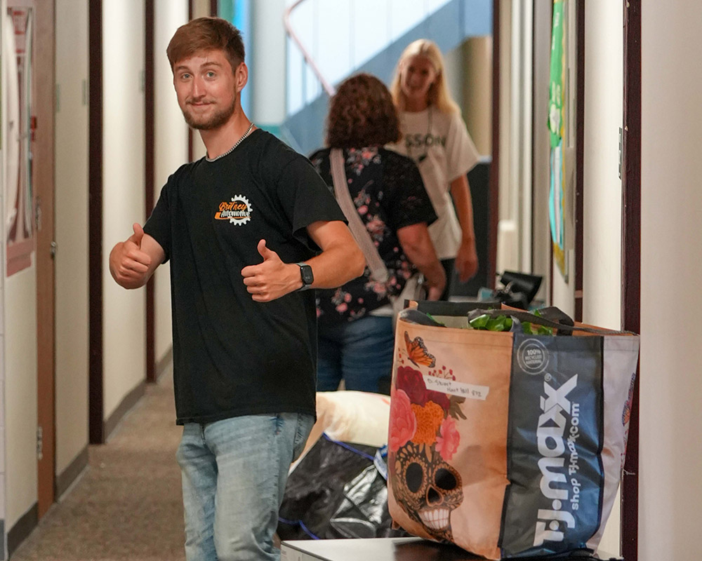 A young man stands in a residence hall hallway smiling at the camera.