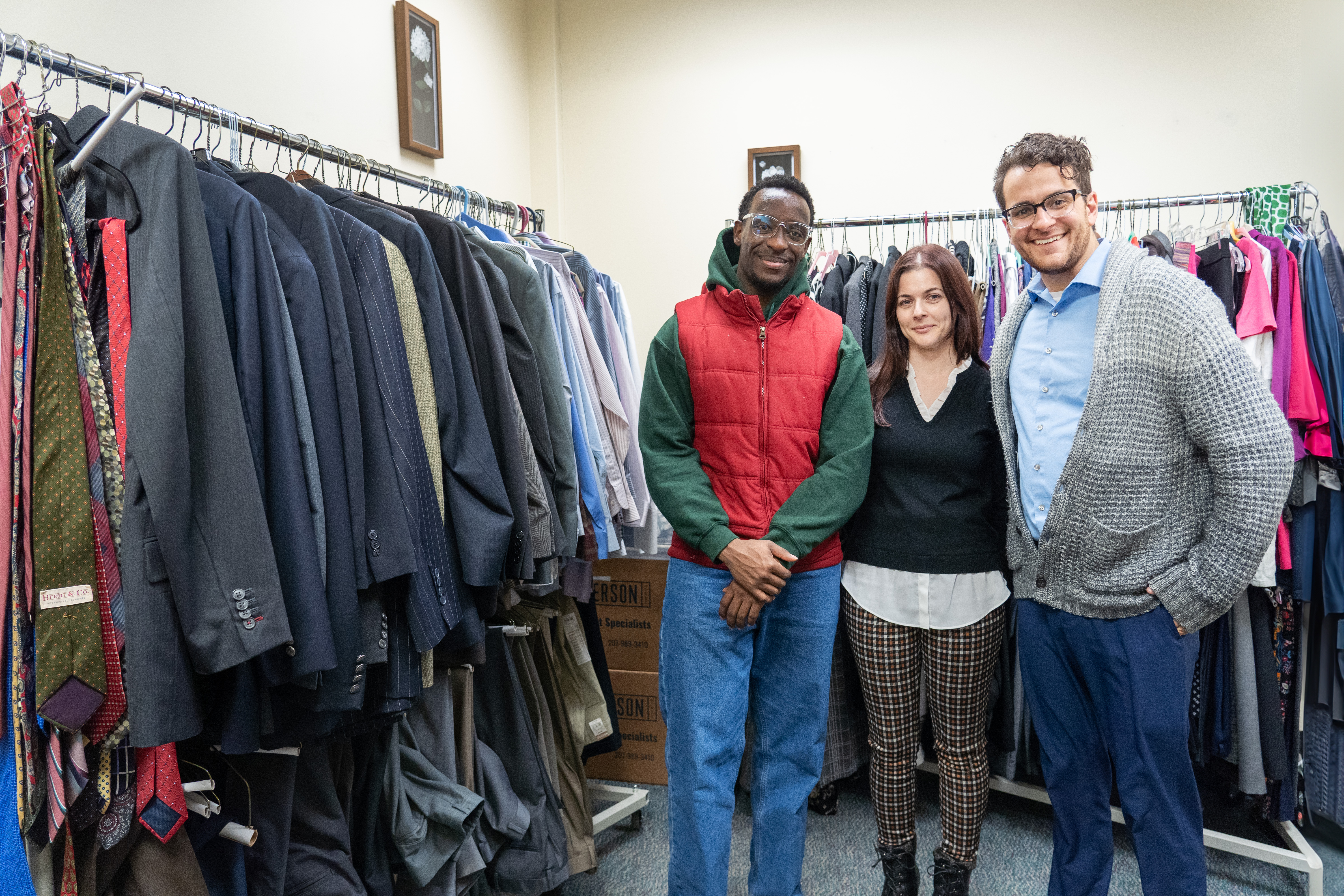 Three smiling people stand in a room filled with clothing.