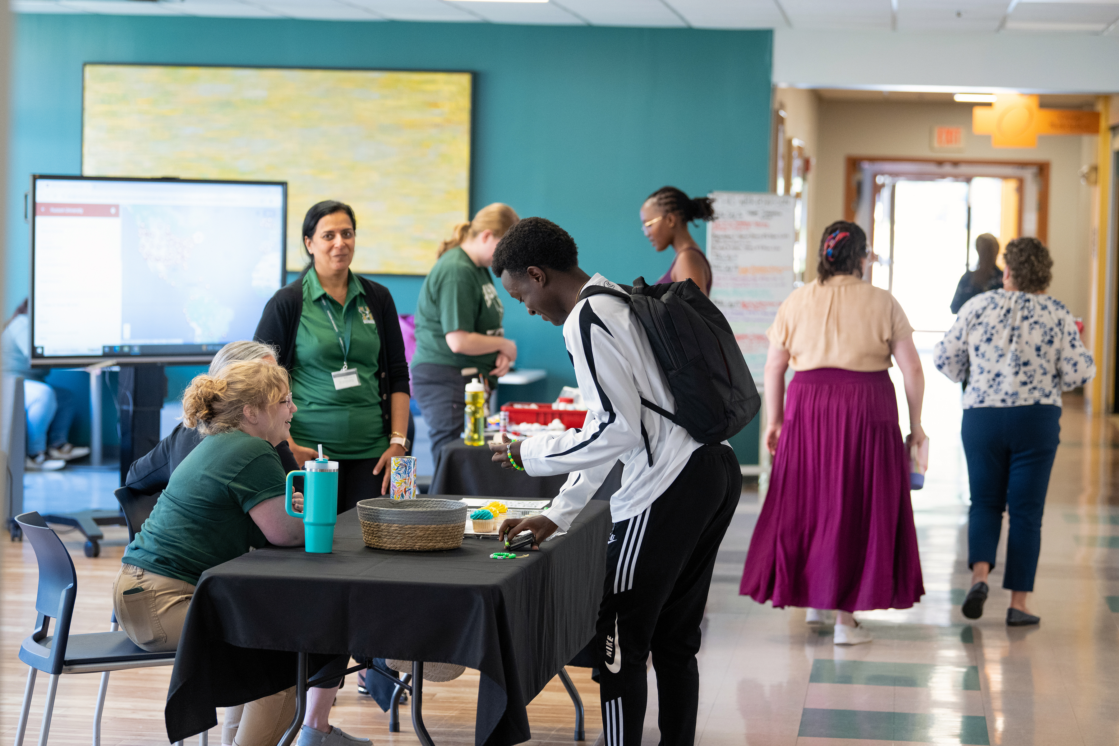 People stand on either sides of tables in a cafeteria.