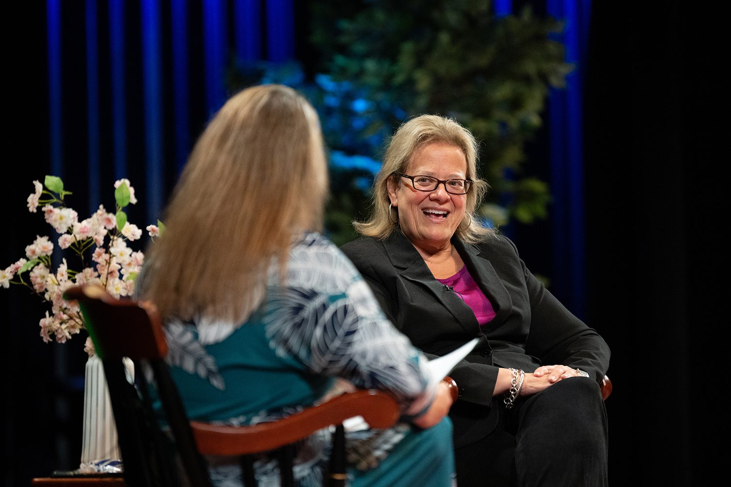 A blond woman smiles at another blond woman while seated on a stage at Husson University.