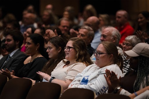 People seated in an audience at The Gracie Theatre at Husson University smile.