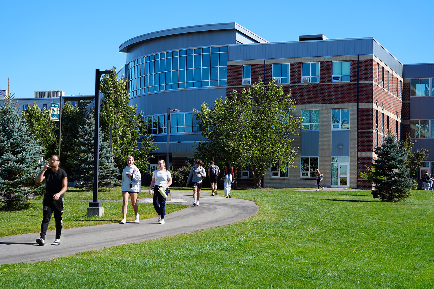 Students walk along a walkway in front of a glass and brick academic building at Husson University.