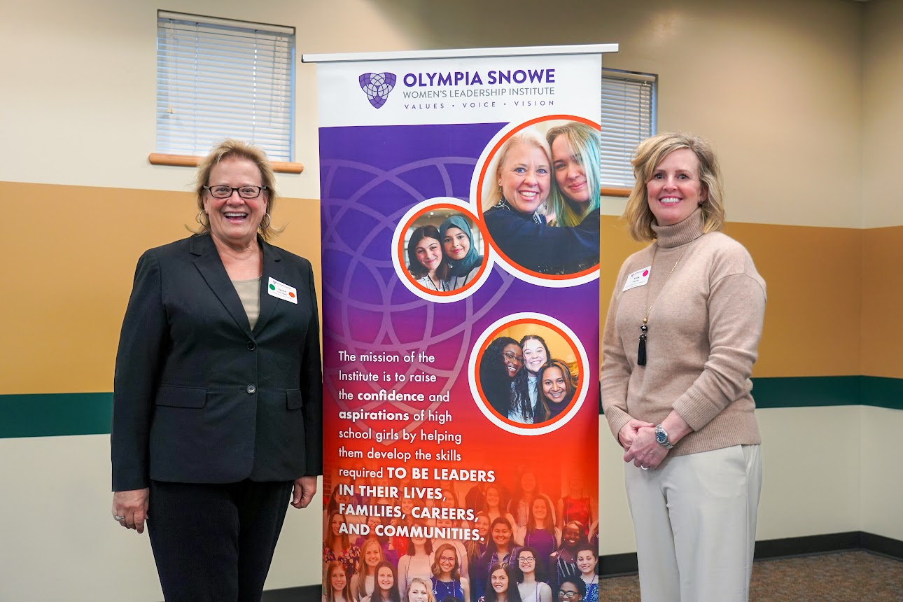 Two women smile at the camera while standing on either side of a banner.