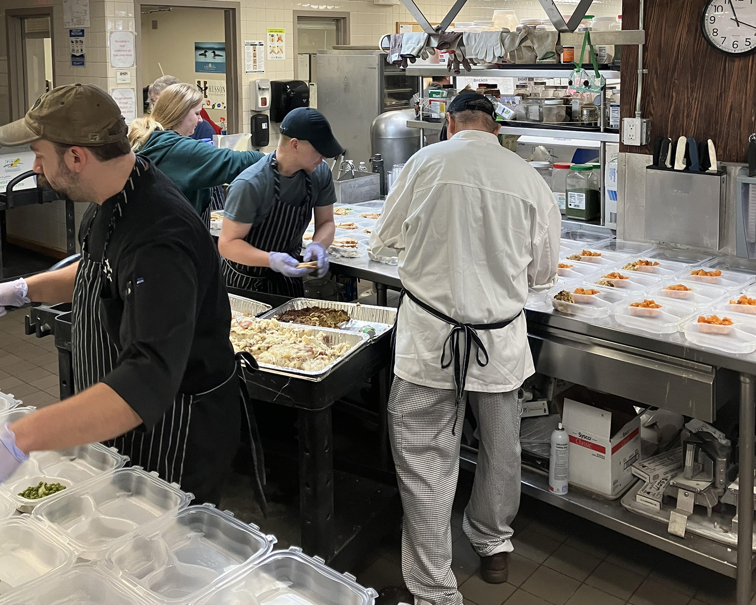 A group of people in a professional kitchen prepare Thanksgiving meals in 2023.