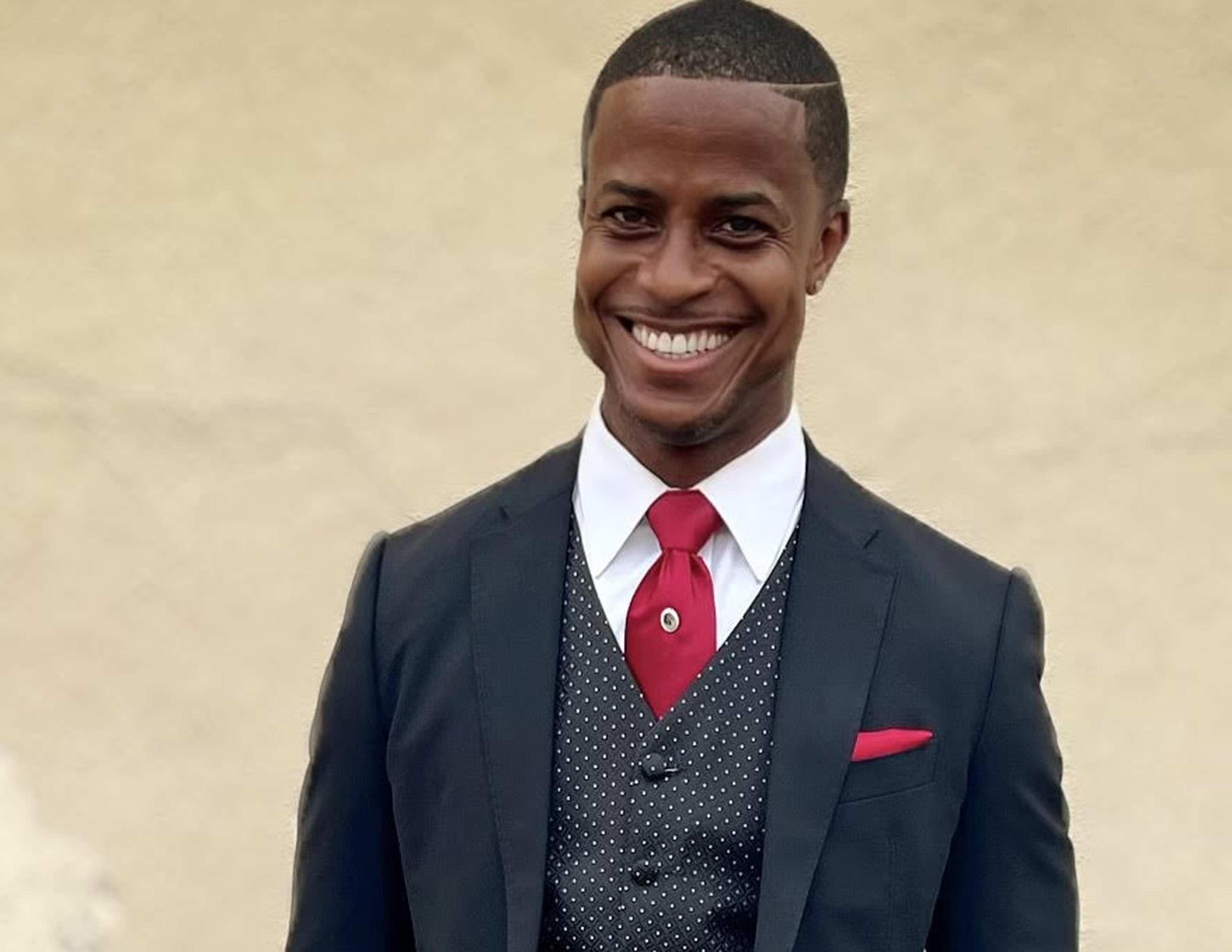 A man in a suit with a red tie and pocket square is shown smiling in this photo.