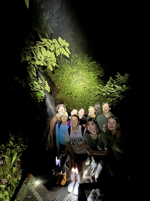 A group of people is shown in a splash of light in a dark outdoor place.