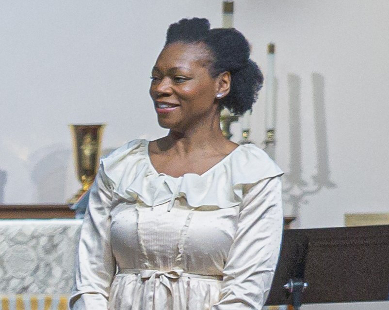 A Black woman in a white dress is shown looking to the side.