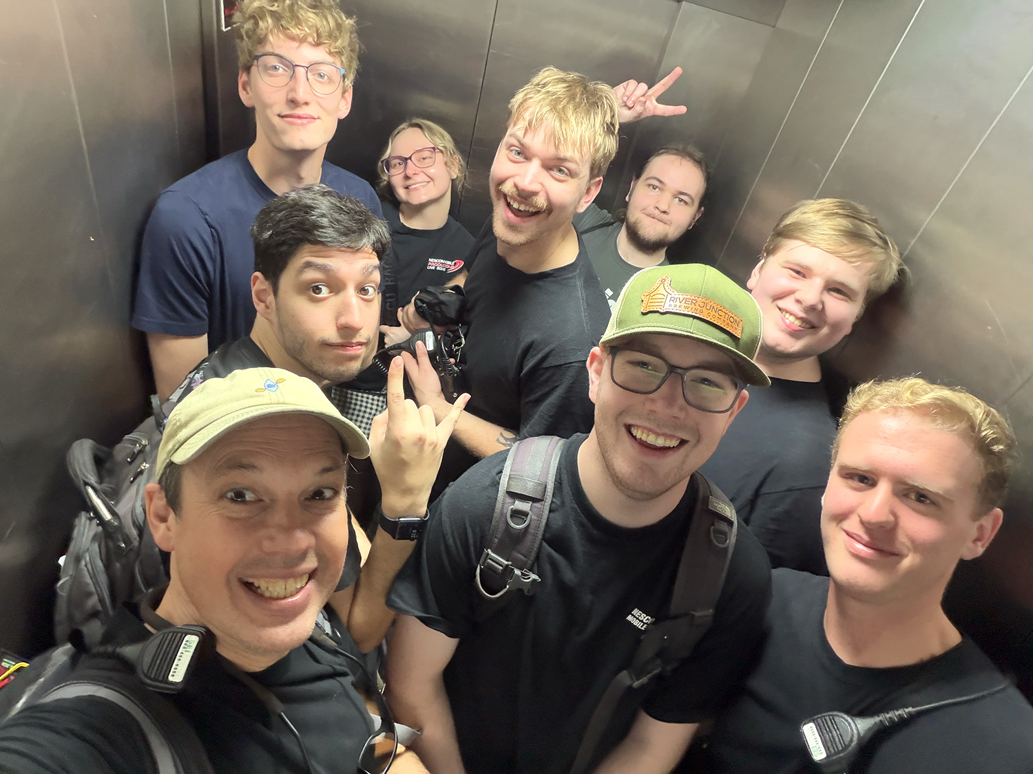 A group of nine people are shown inside a metal elevator.