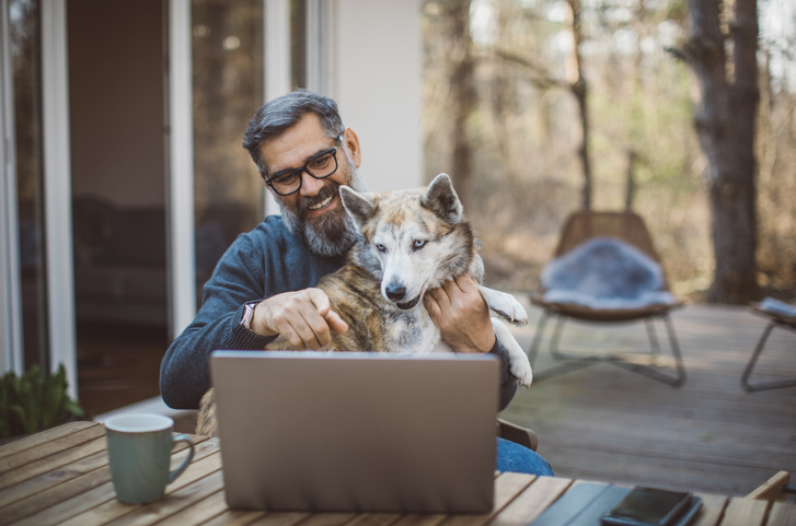 man sitting outside with his dog while working on a laptop computer