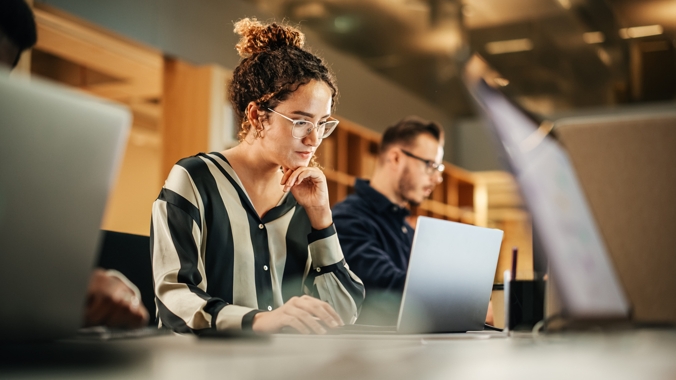 Woman studying on a computer while sitting by other people who are also studying on computers.