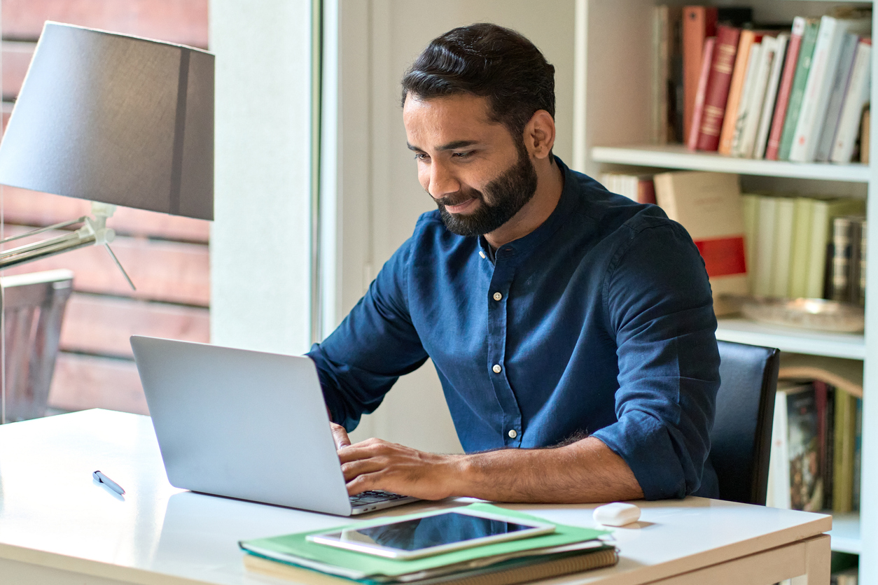 Man works on a laptop while sitting at a desk.