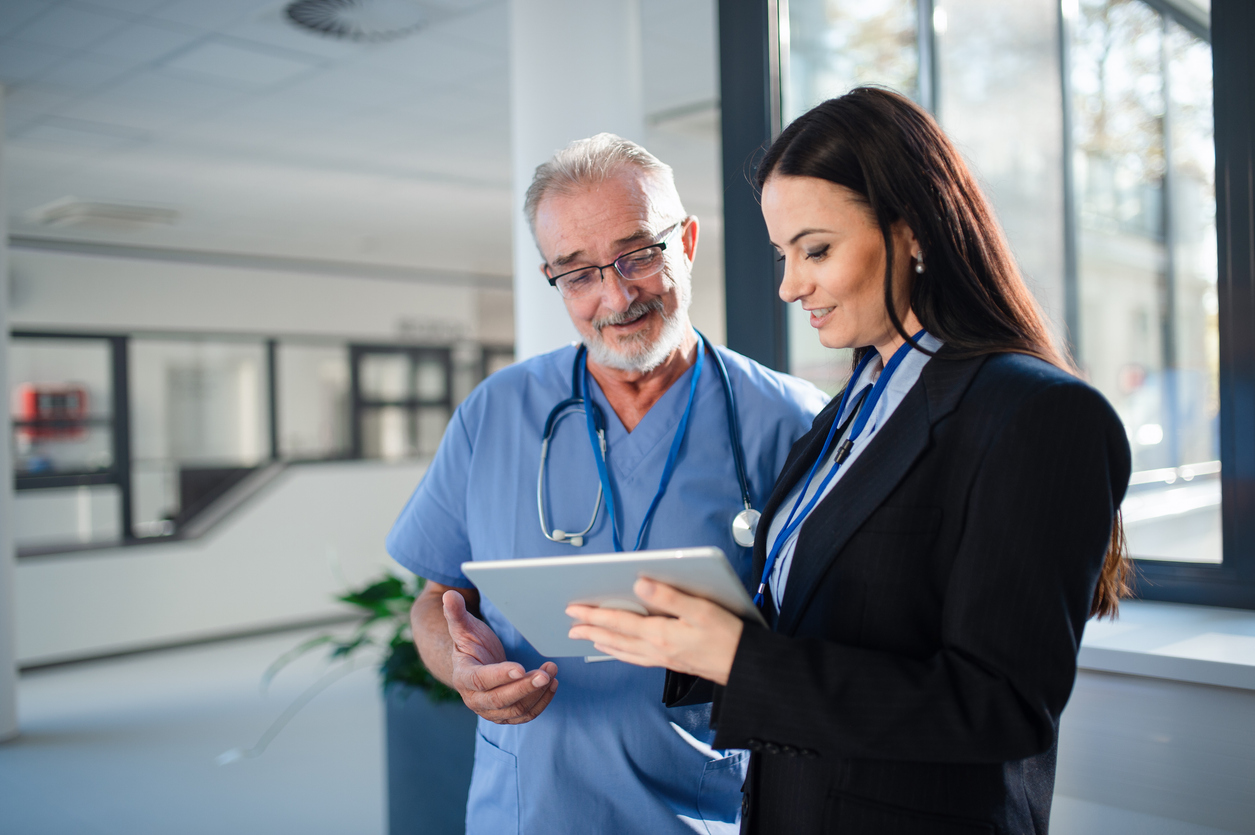 A healthcare administrator speaks with a doctor while pointing at a tablet.