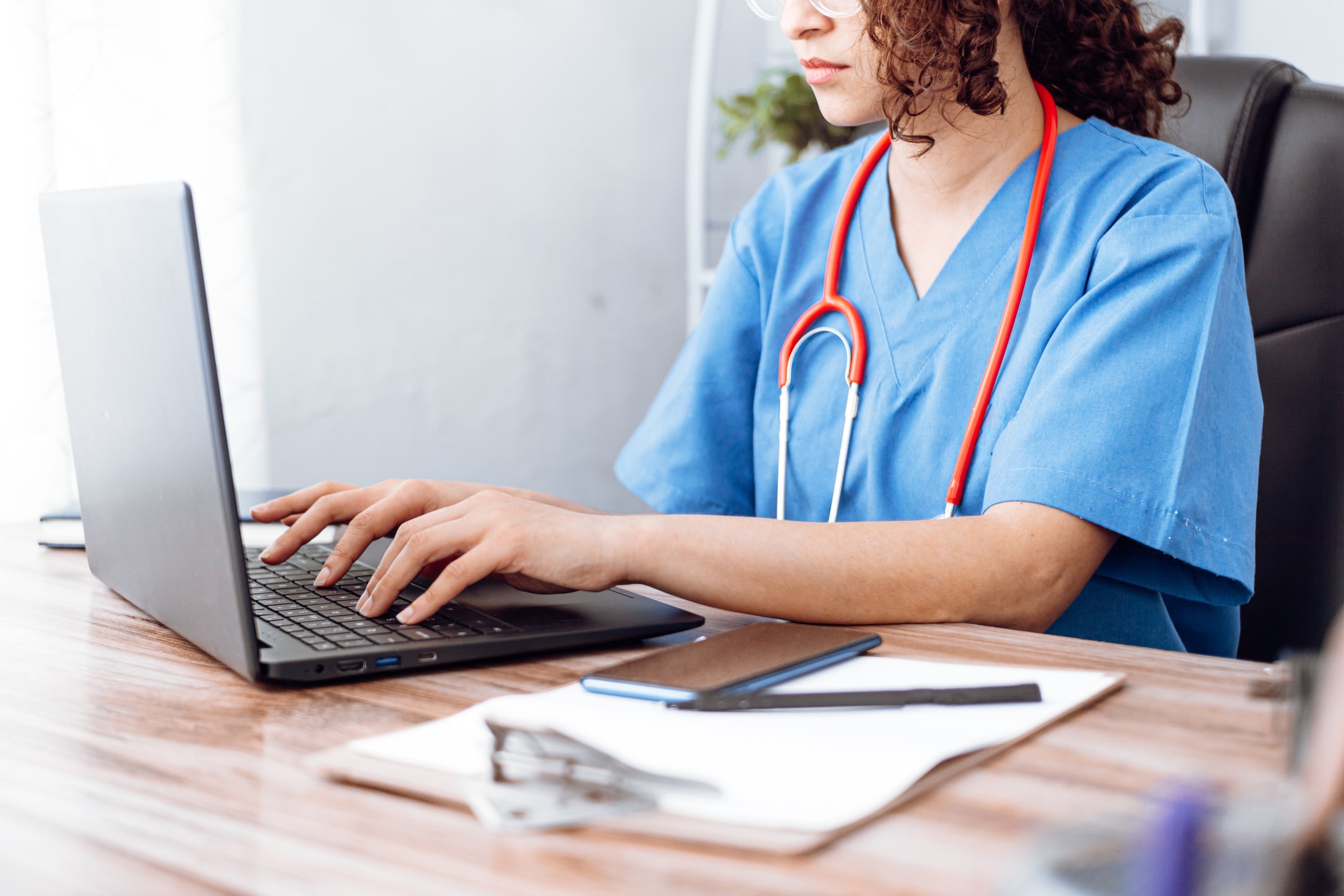 A nurse sitting at a desk while working on a laptop computer.